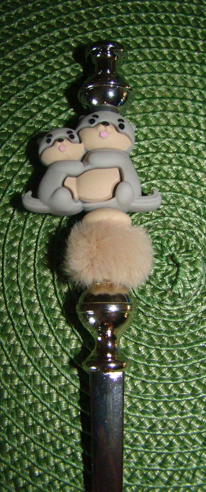 May include: A silver bottle stopper with a furry top and two gray ceramic animal figurines hugging each other.