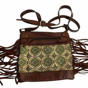May include: Brown leather crossbody bag with a geometric patterned front panel in green and yellow. The bag features long brown fringe along the bottom and sides, a zippered pocket, and an adjustable strap.