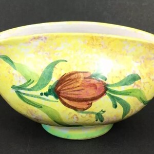May include: A yellow ceramic bowl with a floral design. The bowl has a scalloped edge and a single red flower with green leaves.