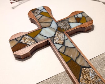 May include: A wooden cross with a mosaic design. The mosaic is made of stained glass in shades of brown, gold, and cream. The cross is a religious item, suitable for home decor or as a gift. The mosaic design has a textured appearance.