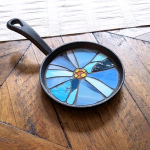 May include: A small cast iron skillet with a blue and yellow mosaic flower design.