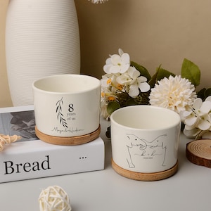 May include: Two cream ceramic plant pots with bamboo saucers. One pot has the text "8 years of us" and the names "Maya & Hudson". The other pot features a line drawing of two elephants and the initials "k + h" with a date.