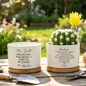May include: Two white ceramic plant pots with bamboo saucers. One contains a cactus with a yellow flower. Text on the pots reads "Mrs. Smith, Thank you for being a part of my story" and "Thank you for listening, for guidance..."