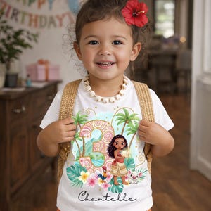 May include: A white t-shirt featuring a graphic of the number three, a cartoon character, a rooster, and a piglet, surrounded by tropical palm trees and flowers. The name Chantelle is printed in black script below the graphic. The shirt is worn with orange patterned shorts and a white shell necklace.