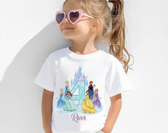 Puede incluir: Camiseta blanca con un gráfico colorido de princesas de Disney, un gran número 4 y un castillo. El nombre "River" está impreso en cursiva debajo del gráfico. La camiseta la lleva una niña pequeña con gafas de sol en forma de corazón.