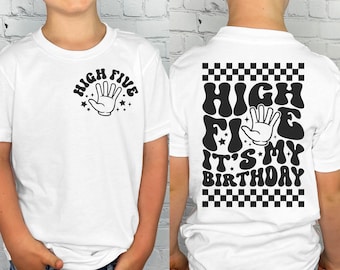 May include: A white t-shirt featuring a black graphic on the front left chest that says HIGH FIVE with a hand icon. The back of the shirt displays a large black graphic with a checkered border, the text HIGH FIVE IT'S MY BIRTHDAY, and a hand icon.