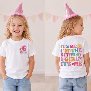 May include: A white t-shirt featuring a pink party hat, blue jeans, and colourful text. The front displays the number 6 and the name Ella. The back features the text: IT'S ME; HI I'M THE BIRTHDAY GIRL IT'S ME, decorated with peace signs and icons.