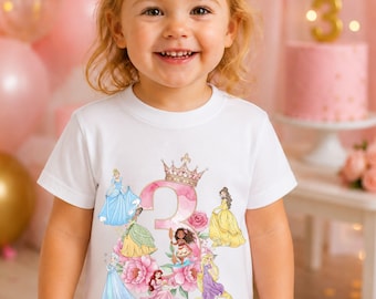 May include: A white short-sleeved t-shirt featuring a large pink watercolor number three topped with a gold crown, surrounded by illustrations of various princesses, pink flowers, and the name Penelope written in pink cursive script below.