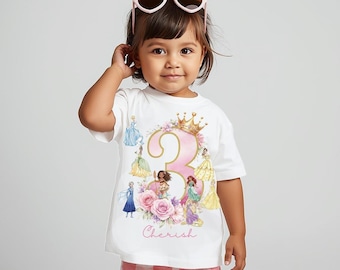 Puede incluir: Una camiseta blanca con un gran número 3 rosa, una corona dorada y detalles florales. La camiseta presenta ilustraciones de princesas y la palabra "Cherish". El niño lleva gafas de sol rosas y pantalones cortos rosas y blancos.