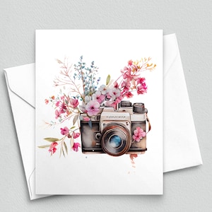 May include: A watercolor illustration of a vintage camera with pink, blue, and white flowers surrounding it.