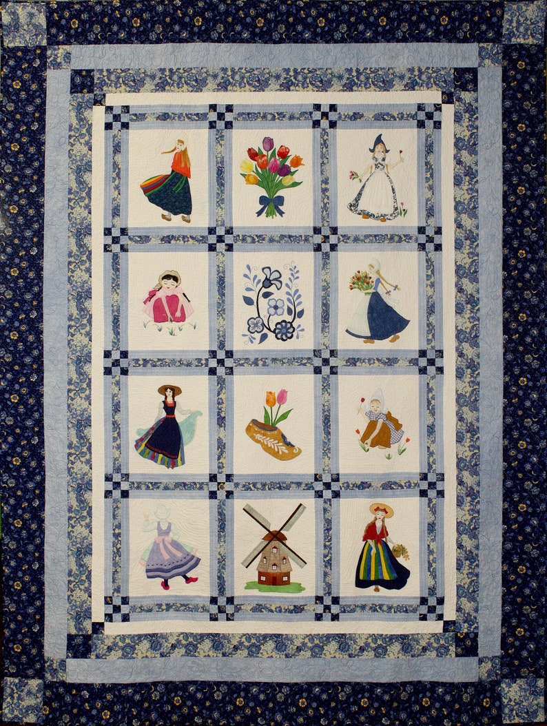 K&ouml;nnte beinhalten: Eine wei&szlig;e Steppdecke mit einem blauen und wei&szlig;en Blumenrand. Die Steppdecke ist in neun Quadrate unterteilt, die jeweils ein anderes gesticktes Design zeigen. Die Designs umfassen ein M&auml;dchen in einem blauen Kleid, eine Windm&uuml;hle, einen Tulpenstrau&szlig; und ein Paar Holzschuhe.