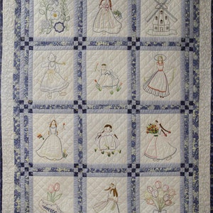 K&ouml;nnte beinhalten: Eine wei&szlig;e Steppdecke mit einem blau-wei&szlig;en Blumenmuster. Die Steppdecke ist in neun Quadrate unterteilt, jedes mit einem anderen Stickmuster. Die Muster umfassen eine Windm&uuml;hle, Blumen und M&auml;dchen in traditioneller niederl&auml;ndischer Kleidung.