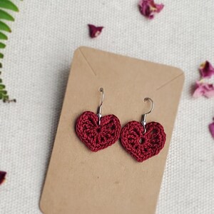 May include: A pair of maroon crocheted heart-shaped earrings with silver hooks.