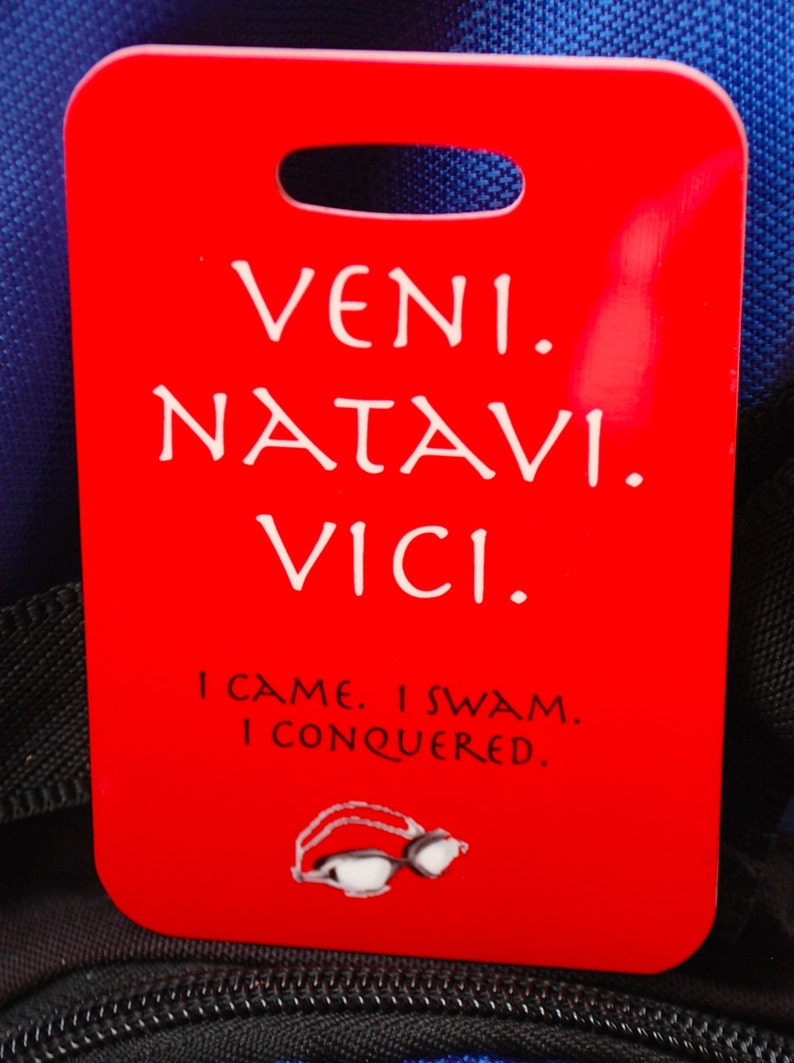 May include: Red luggage tag with the Latin phrase "veni, natavi, vici" and the English translation "I came, I swam, I conquered".