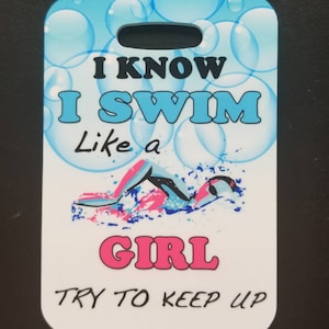 May include: White rectangular tag with a blue and white bubble background. The tag has a hole at the top for hanging. The text on the tag reads "I know I swim like a girl try to keep up". The text "girl" is in pink. A cartoon image of a swimmer is in the center of the tag.