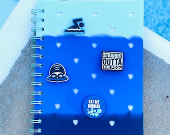 May include: A spiral-bound notebook with a blue gradient cover, decorated with swimming-themed charms. The notebook features heart-shaped cutouts and the phrases "STRAIGHT OUTTA THE POOL" and "EAT MY BUBBLES".