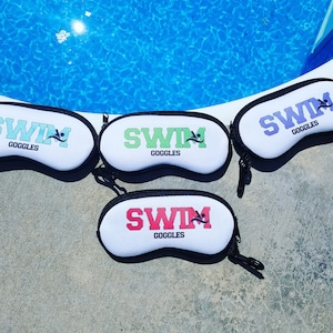 May include: Four white zippered pouches with black trim and the words "Swim Goggles" printed on them. Each pouch has a different colored word "Swim" in green, blue, pink, and purple.