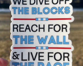 May include: A white sticker with black and light blue text that reads "WE DIVE OFF THE BLOCKS REACH FOR THE WALL & LIVE FOR THE RACE." The sticker has a red stripe with blue and white accents.