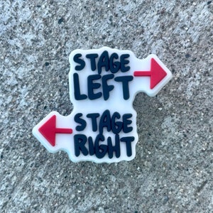 May include: White sticker with black text and red arrows. The text reads "Stage Left" with a right-facing arrow and "Stage Right" with a left-facing arrow.