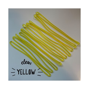 May include: A close-up of ten bright yellow rubber bands, all neatly stacked on top of each other. The text "clear YELLOW" is written in black marker below the rubber bands.