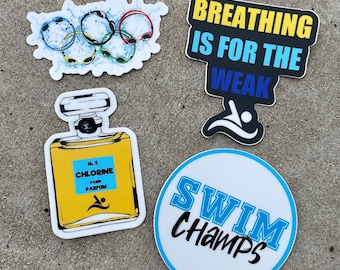 May include: Four stickers with swimming-themed designs. The first sticker is a blue and yellow Olympic rings with water splashes. The second sticker is black with yellow and blue text that reads "Breathing is for the weak" with a blue swimmer icon. The third sticker is a yellow and white perfume bottle with the text "No. 5 Chlorine Paris Parfum" and a blue swimmer icon. The fourth sticker is a white circle with a blue border and the text "Swim Champs" in blue and black.