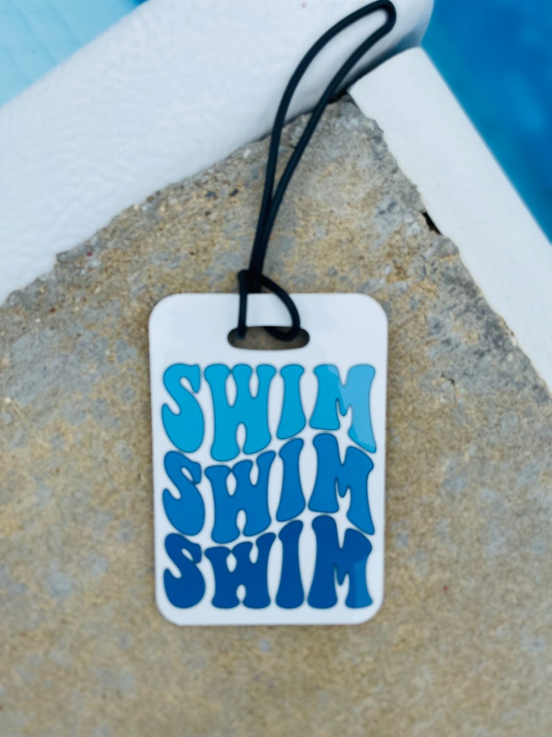 Puede incluir: Etiqueta de equipaje blanca con un dise&ntilde;o azul degradado que dice "Swim" tres veces.