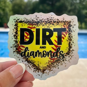May include: A yellow and red softball with a black outline and the words "Dirt and Diamonds" in black script. The softball is surrounded by a black and white speckled background.