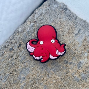 May include: A red octopus with pink tentacles and white eyes. The octopus is made of rubber and has a cartoonish appearance.