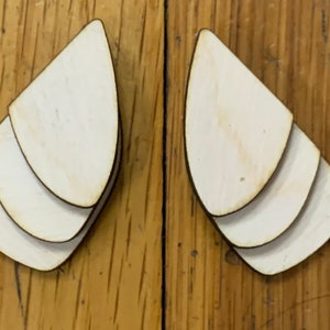 May include: A pair of white wooden earrings with a layered teardrop design.