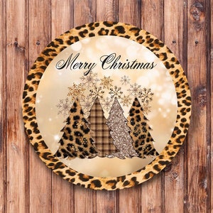 May include: Round Christmas ornament with a leopard print border. The center features a gold background with three Christmas trees decorated with leopard print, plaid, and glitter. The text "Merry Christmas" is written in a cursive font above the trees.