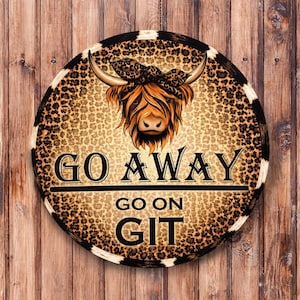 May include: Round wooden sign with a brown and tan leopard print background. The sign features a Highland cow illustration with a bandana and the words "GO AWAY GO ON GIT" in black lettering.