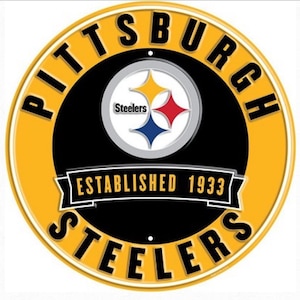 May include: Circular sign featuring the Pittsburgh Steelers logo. The logo includes a black circle with the team name in yellow around the edge. The center has the Steelers logo with a yellow, red, and blue star.