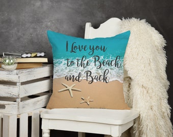 May include: A square cushion featuring a beach design. The cushion has a turquoise blue sky and ocean, a sandy beach, and two starfish. The text "I love you to the Beach and Back" is printed on the cushion.