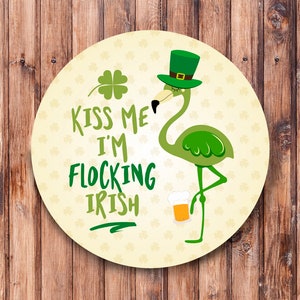 May include: A round, white and green coaster with a green flamingo wearing a green hat and holding a glass of beer. The text on the coaster reads "Kiss me I'm flocking Irish".