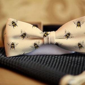 May include: A white bow tie with a pattern of yellow and black bees. The bow tie is on a black and white patterned surface.