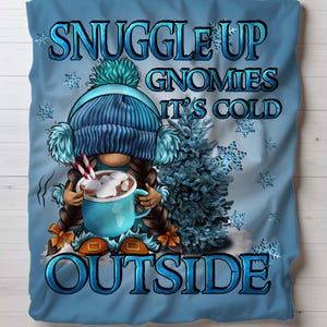 May include: A blue and white gnome with a blue hat and a cup of hot chocolate with marshmallows. The gnome is sitting in front of a blue Christmas tree with the text "Snuggle Up Gnomies It's Cold Outside".