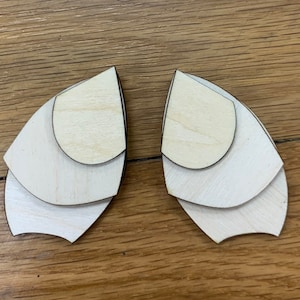 May include: A pair of wooden earrings with a layered design. Each earring is made of three overlapping pieces of wood, creating a unique and modern look.