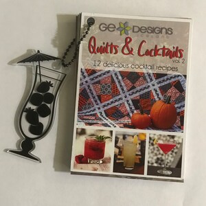 May include: A book titled "Quilts & Cocktails Vol. 2" with 12 delicious cocktail recipes. The cover features a quilt design, pumpkins, and photos of cocktails.