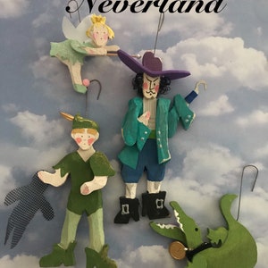 Peut inclure: Ornements en bois peints à la main représentant des personnages de Peter Pan, dont Peter Pan, le Capitaine Crochet, une fée et un crocodile. Le mot "Neverland" est écrit en haut. Les ornements sont de couleurs vives et ont des cintres en fil de fer.