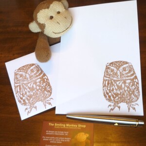 May include: Two brown owl illustrations on white envelopes with a brown stuffed monkey and a silver pen on a wooden surface. The envelopes have the text "The Smiling Monkey Shop" printed on them.