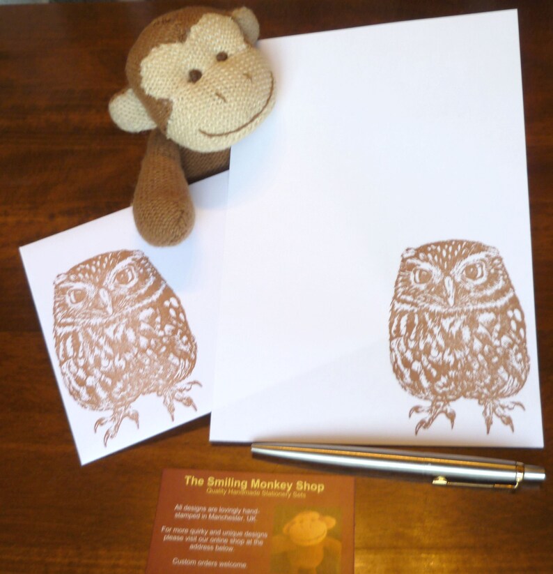 May include: Two brown owl illustrations on white envelopes with a brown stuffed monkey and a silver pen on a wooden surface. The envelopes have the text "The Smiling Monkey Shop" printed on them.