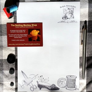 Puede incluir: Un juego de papeler&iacute;a con una hoja de papel blanca con un dise&ntilde;o de costura impreso, una tarjeta de visita y un bol&iacute;grafo. La tarjeta de visita dice "The Smiling Monkey Shop" e incluye una peque&ntilde;a ilustraci&oacute;n de un mono. Tambi&eacute;n se incluyen carretes de hilo y botones.