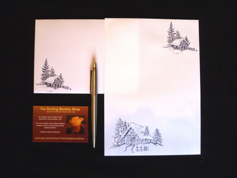 May include: A set of white stationery featuring a black and white illustration of a cabin in the woods. The stationery includes a letterhead, envelope, and business card. The business card has the text "The Smiling Monkey Shop" and a cartoon monkey.