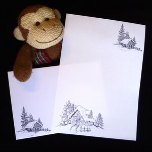 May include: Two white cards with black ink drawings of a cabin in a snowy forest. The cards are blank and ready to be written on.