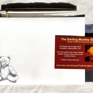 May include: A white envelope with a hand-drawn illustration of a teddy bear. A red business card with the text "The Smiling Monkey Shop" and the website address "www.etsy.com/uk/shop/TheSmilingMonkeyShop" is on top of the envelope.