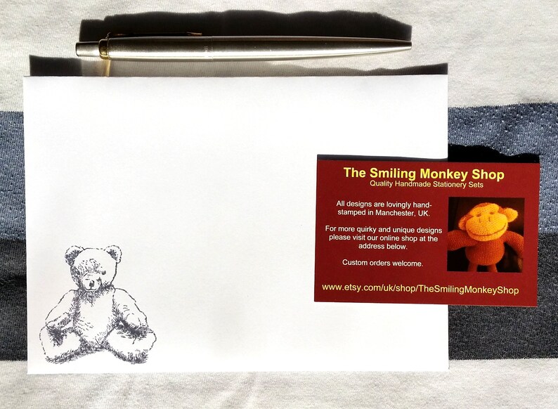 May include: A white envelope with a hand-drawn illustration of a teddy bear. A red business card with the text "The Smiling Monkey Shop" and the website address "www.etsy.com/uk/shop/TheSmilingMonkeyShop" is on top of the envelope.