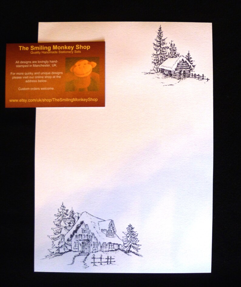May include: A black and white illustration of a snowy cabin with a snow-covered roof. The cabin is surrounded by trees and a fence. The text "The Smiling Monkey Shop" is printed on the top of the image.