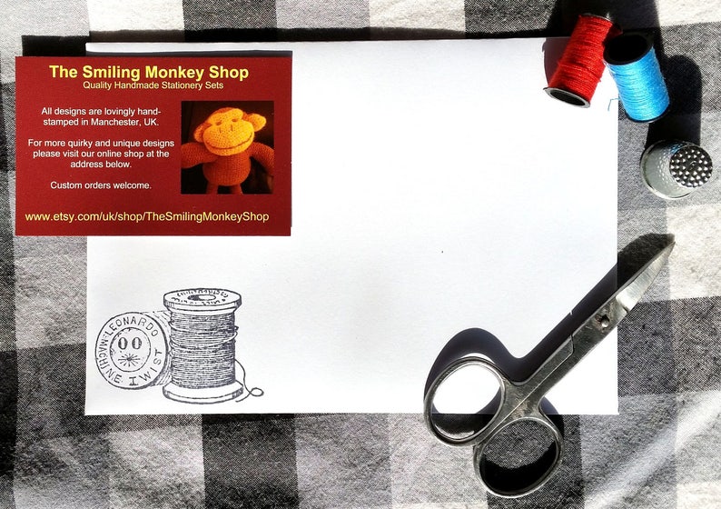 Puede incluir: Un juego de papeler&iacute;a blanco con una tarjeta de visita roja y naranja de The Smiling Monkey Shop. El juego incluye carretes de hilo rojo y azul, un dedal, tijeras y una imagen estampada de una bobina de hilo.