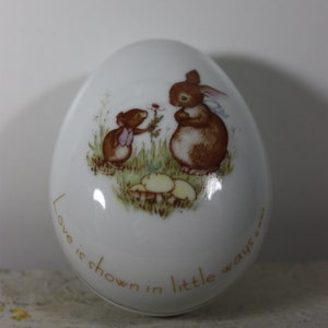 May include: White porcelain egg-shaped trinket box with a brown rabbit and a mouse holding a flower. The box has the text "Love is shown in little ways" around the bottom.