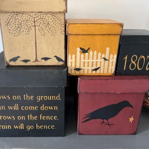 May include: A collection of decorative boxes with various designs. One box features a tree and crows, another has a fence and birds, and a third displays the number 1807. Additional boxes have crow illustrations and text: "Crows on the ground, rain will come down, Crows on the fence, rain will go hence."